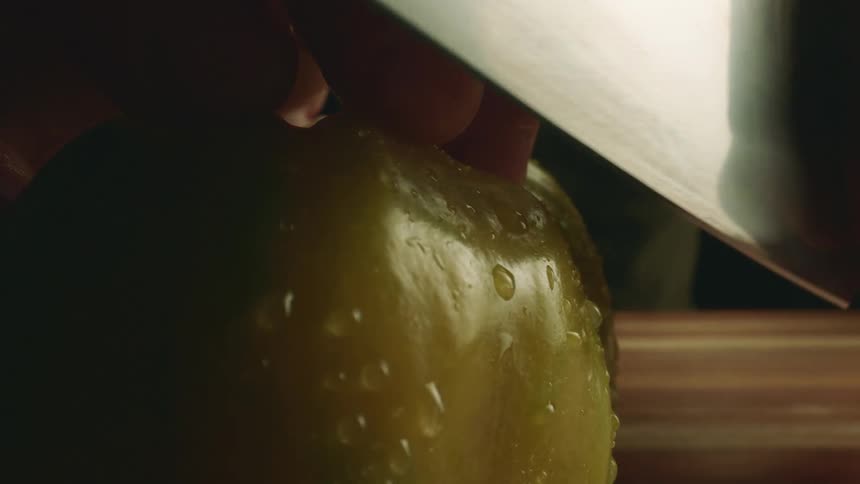 Close up of a tattoed man cutting tomatoes with a sharp kitchen knife over a wooden board