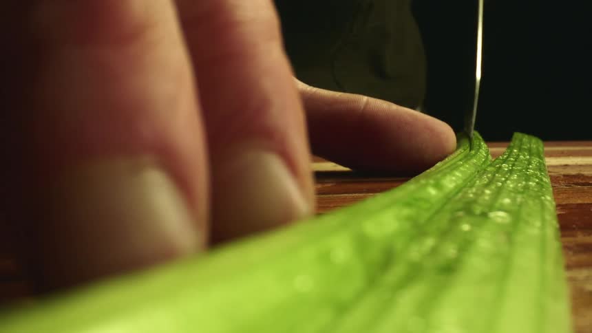 A sharp knife cutting through a piece of celery on a wood cutting board