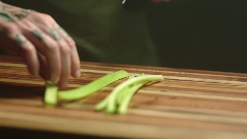 A person cutting a vegetable with a knife on a cutting board
