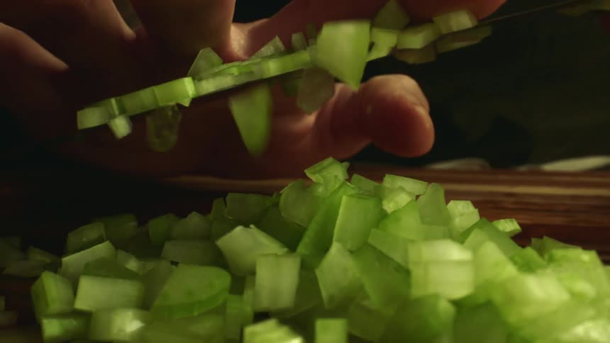 A person removing chopped vegetables from their knife