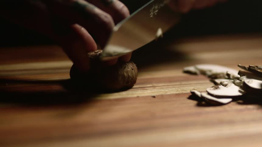 A man slices mushrooms on a cutting board with a sharp knife