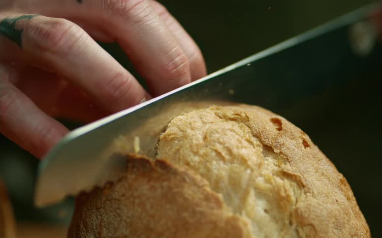 A person cutting bread with a knife with crumbs flying