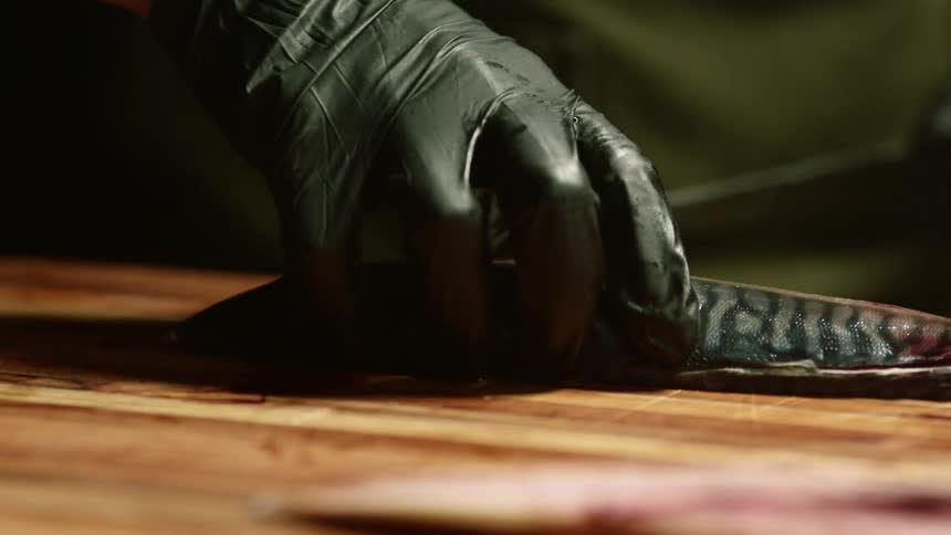 A chef wears black gloves while slicing a long fish