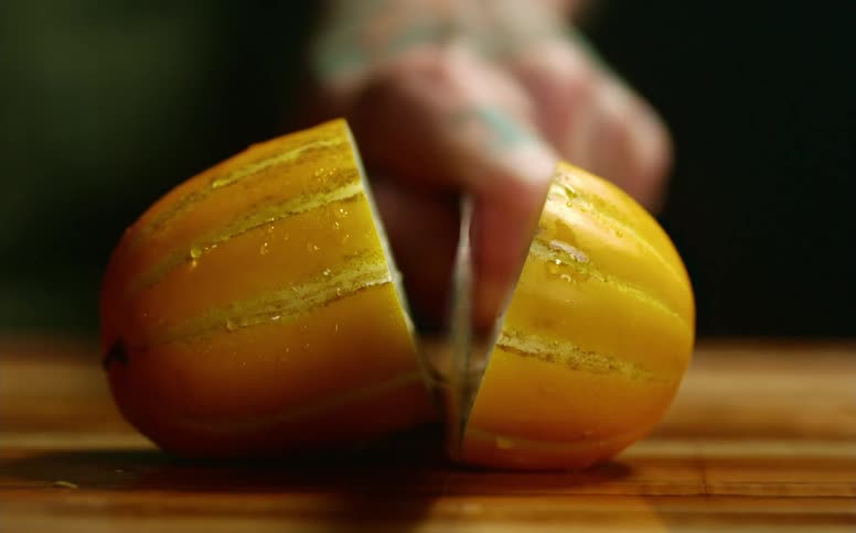 A man uses a sharp knife to slice a squash in half on a wooden cutting board