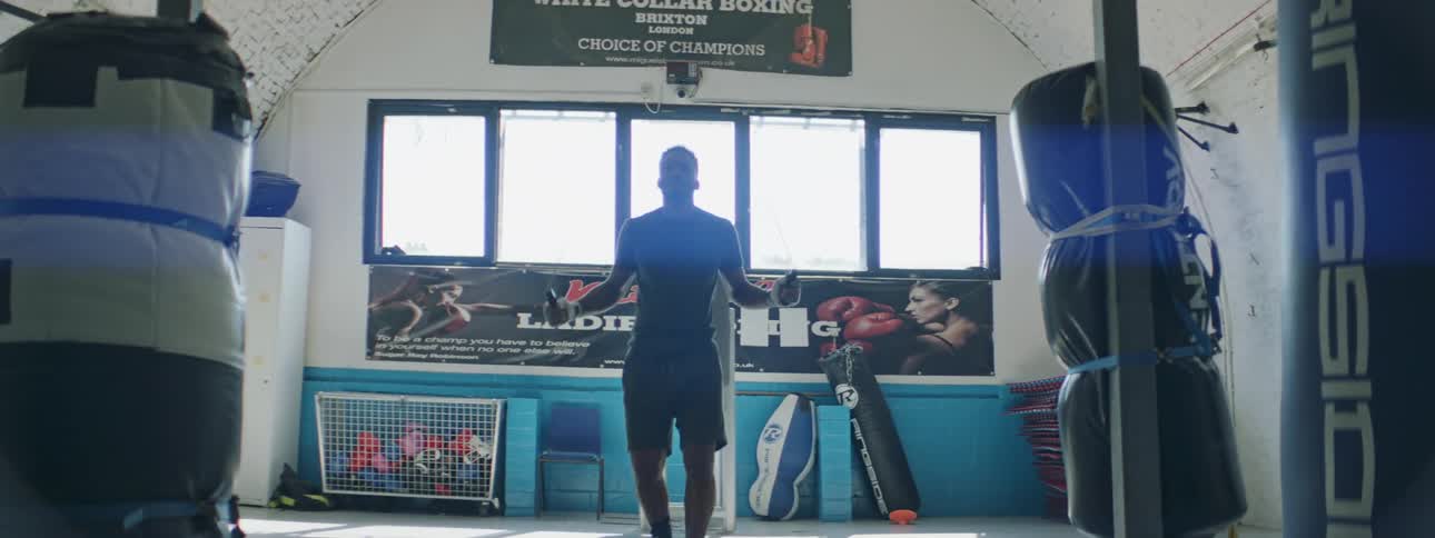 A man jumps rope in a gym near large boxing bags