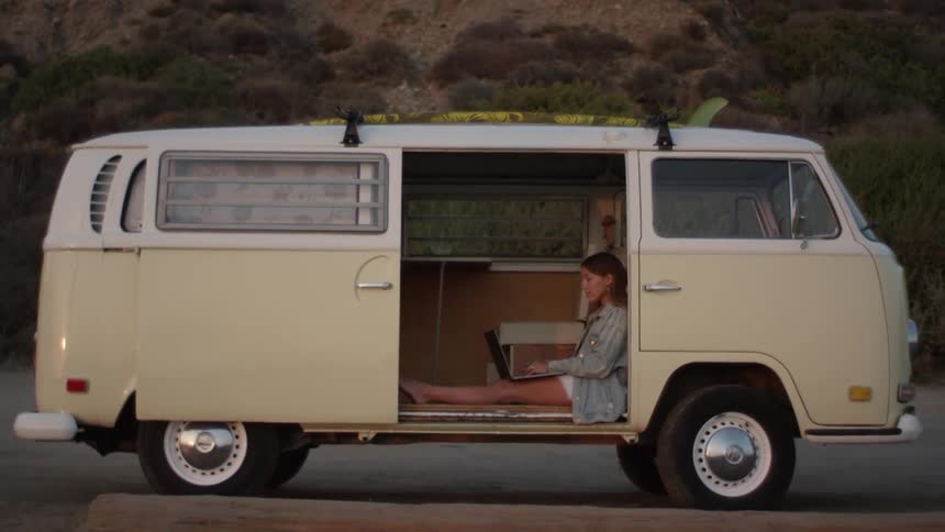 A woman sits in the open side door of a van while she types on her laptop