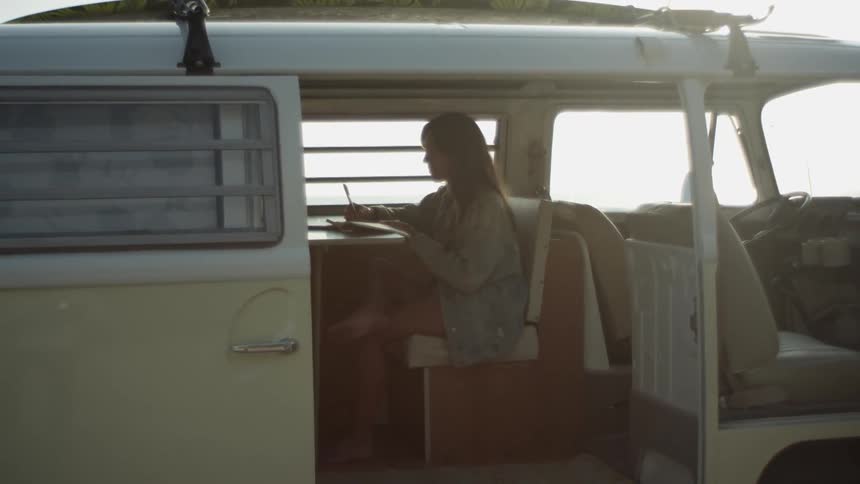 A woman writing in a notebook while sitting inside a van with an open door