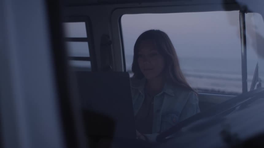 A woman is typing on the laptop inside the van