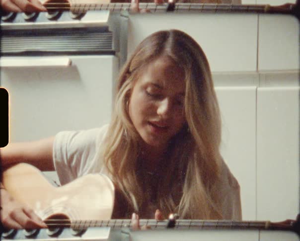 A woman sitting on the kitchen floor playing guitar and singing