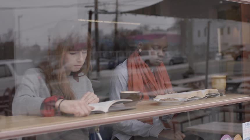 Two people are sitting by a window table reading