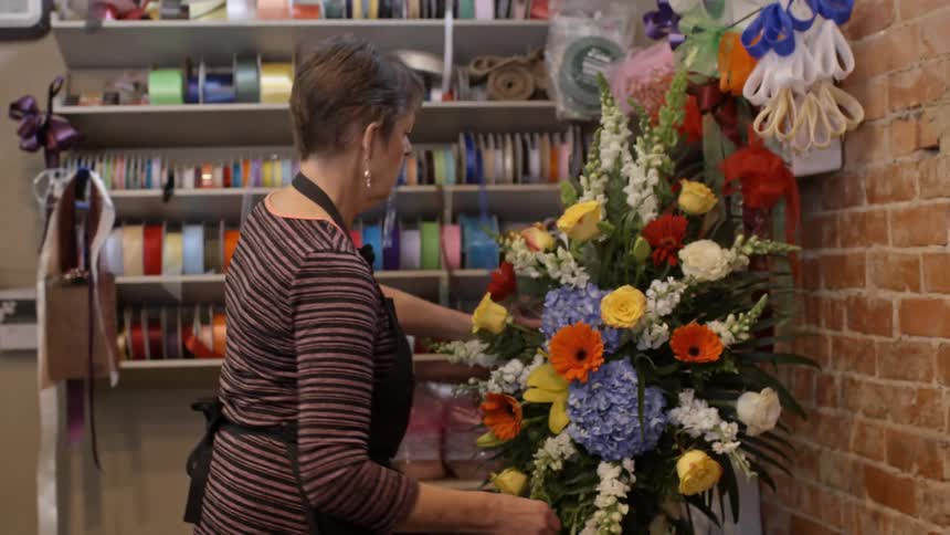 A woman walks over and puts a flower in an arrangement