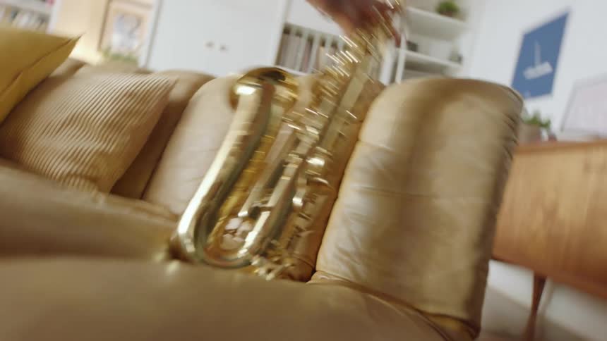 A person retrieves a saxophone resting on the seat of a leather sofa in the living room of a house