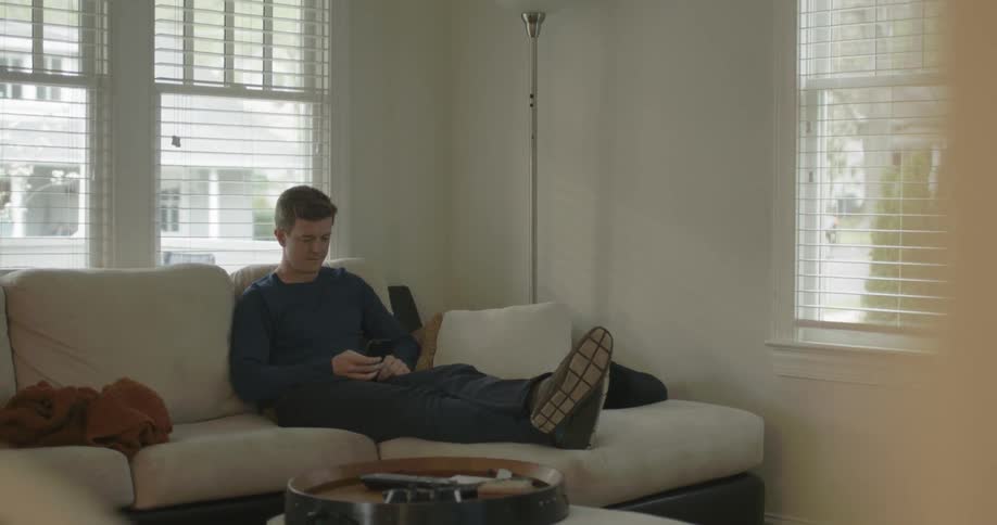 A man sits on his couch looking at his cellphone during the day