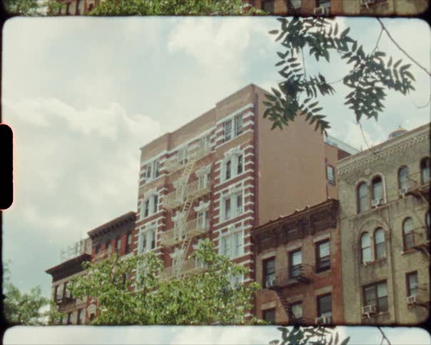 Buildings with fire escapes with trees in the foreground and the sky and clouds in the background