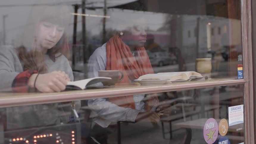 People are sitting inside a restaurant window reading