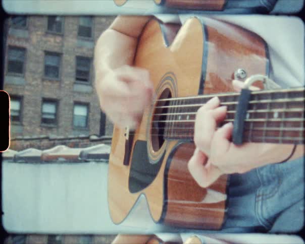 A guitarist plays the guitar while standing on the rooftop of a building in a city during the day