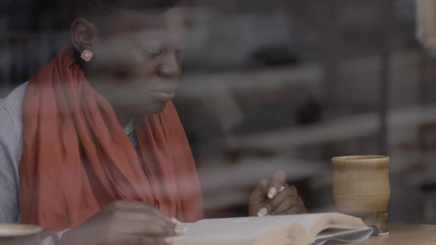 A woman in an orange scarf reads in a cafe
