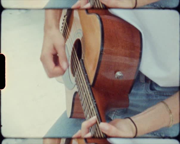 A woman wearing blue jeans and a tee shirt plays guitar