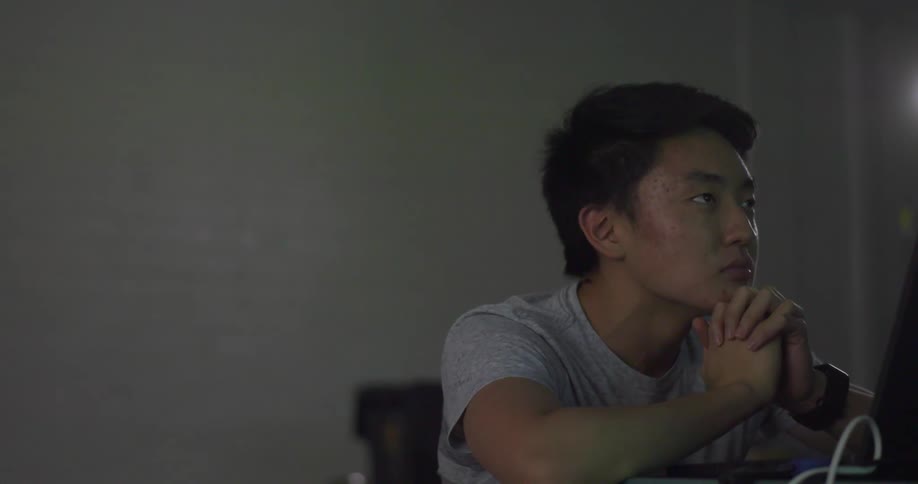 Man sits with clasped hands at table looking at screen