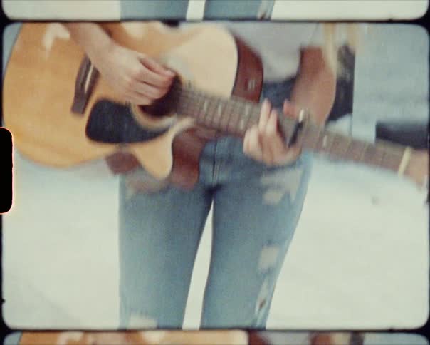 A young woman plays a guitar while standing outdoors on a sunny day