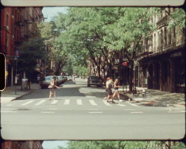 People cross a city street at an intersection alongside vehicles and bicyclists