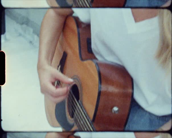 A woman plays guitar outside with brick city buildings behind her