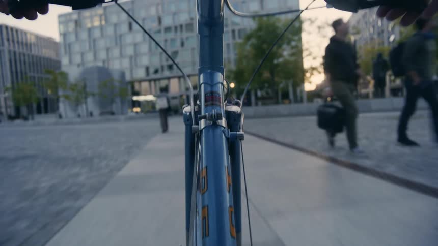 Person rides bicycle along sidewalk in city passing pedestrians