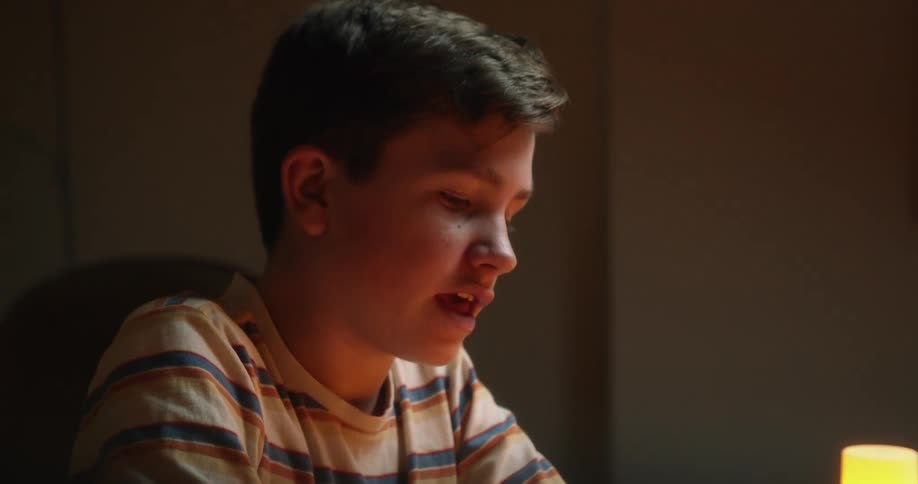 A boy in a striped shirt singing to himself indoors