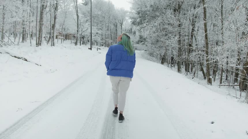A teenage girl walks along a snowy covered road next to a forest