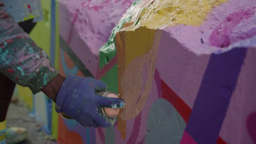 A painter uses spray paint to paint a ruined wall outdoors during the day