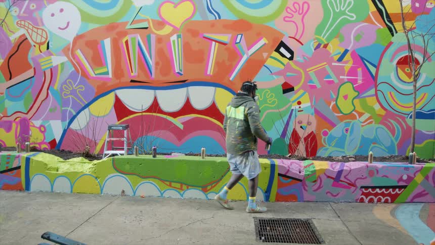 Artist steps away from mural painted on wall and flower bed retaining wall