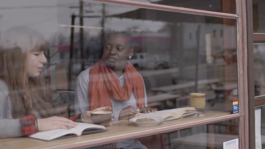 Two women read and drink coffee behind a window