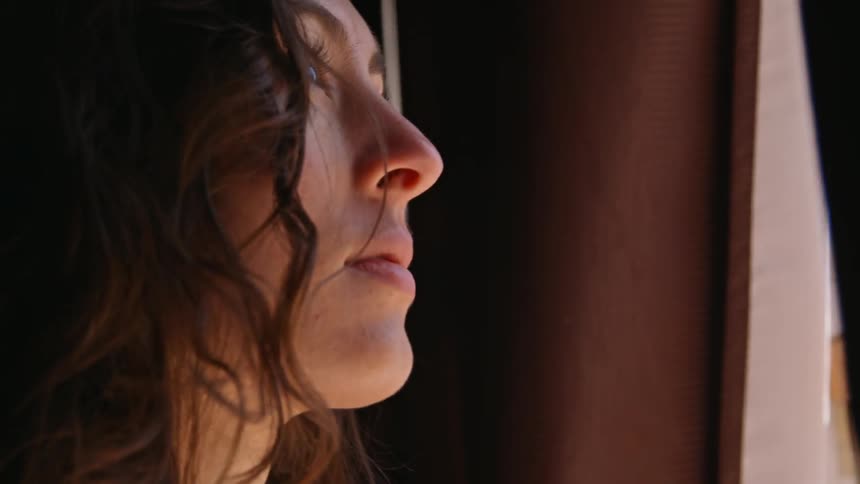 A woman peeks through window drapes