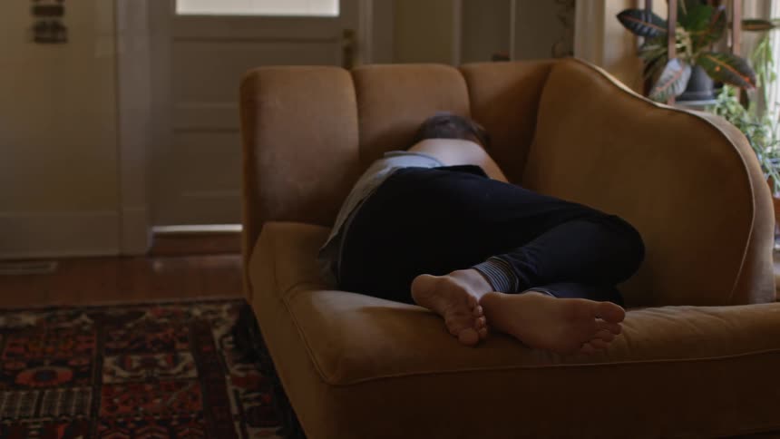 A cat watches as a man sleeps on the couch