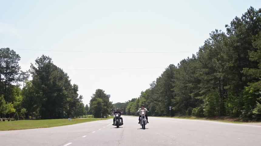 Two men driving motorcycles along a road