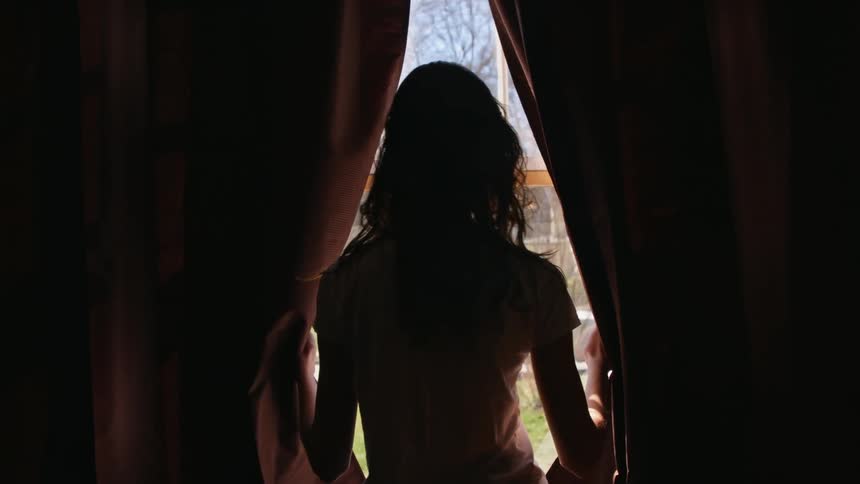 A woman opening drapes to look out a window