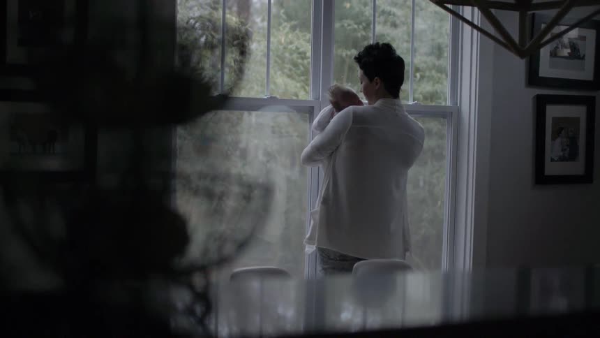 A woman holds a baby in front of a window