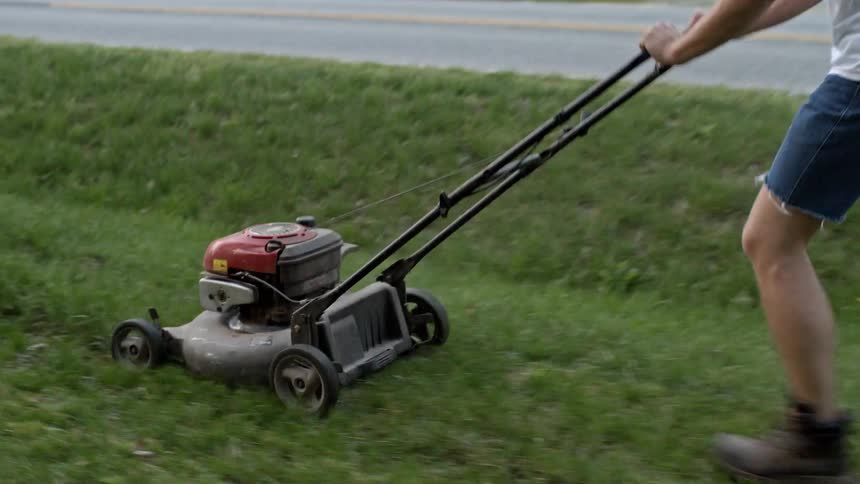 A man mows his lawn in denim cutoffs