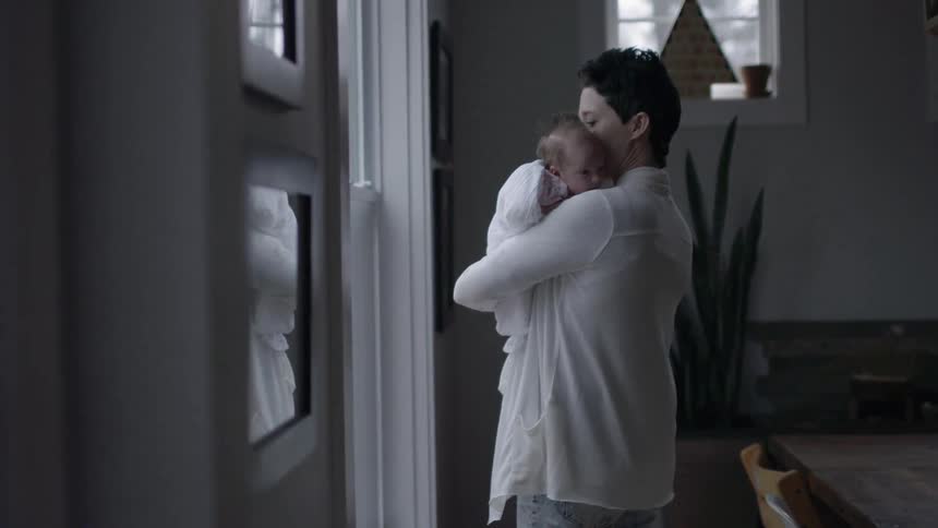 A woman is holding a baby in her arms by a window