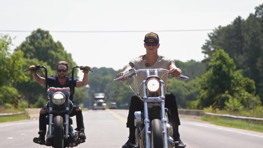 Motorcyclists ride on a rural road on a sunny day