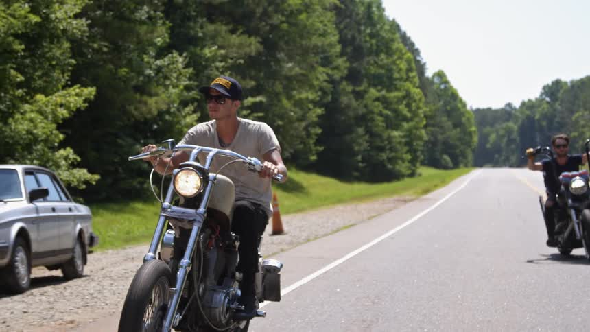 Two men ride motorcycles through a forested road