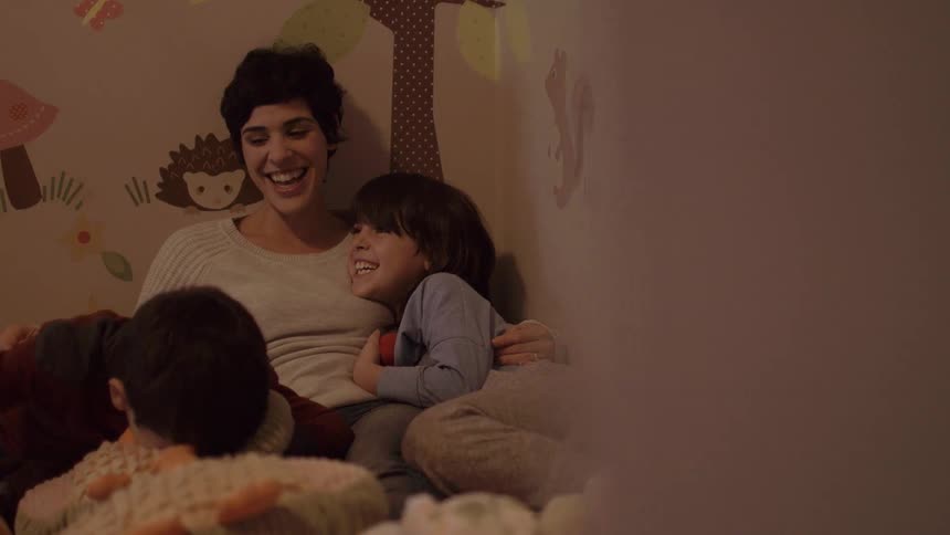 A woman is laughing with two children in bed