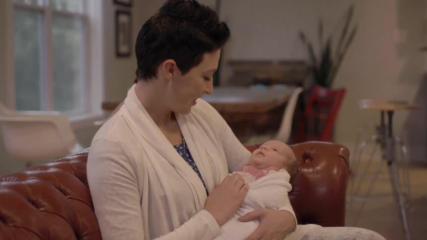 A woman holds a newborn on a couch in her home