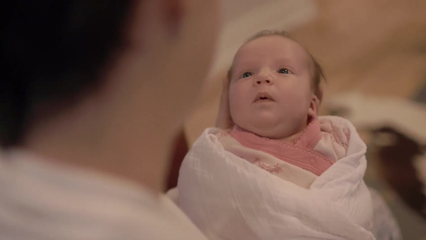 A person holds a young baby that is swaddled in a blanket