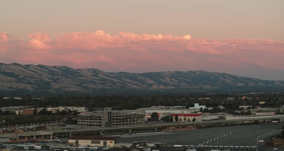 City buildings and highway with mountains in the background under a pink sky