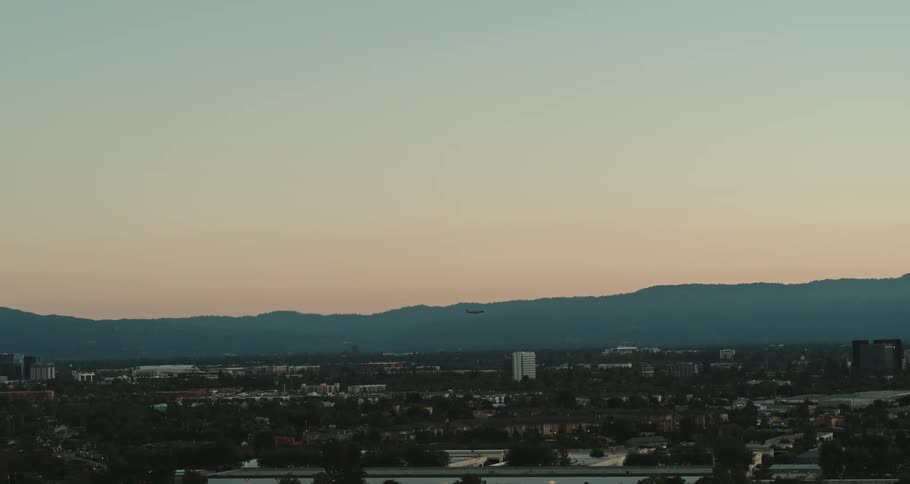 City with may buildings and mountains on the horizon and an airplane flying in the distance
