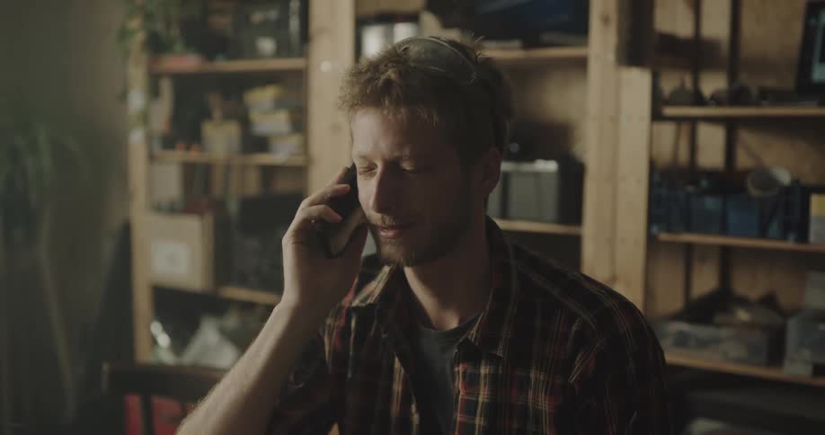 A man talks on his smartphone while sitting in his garage in front of a large wooden shelf