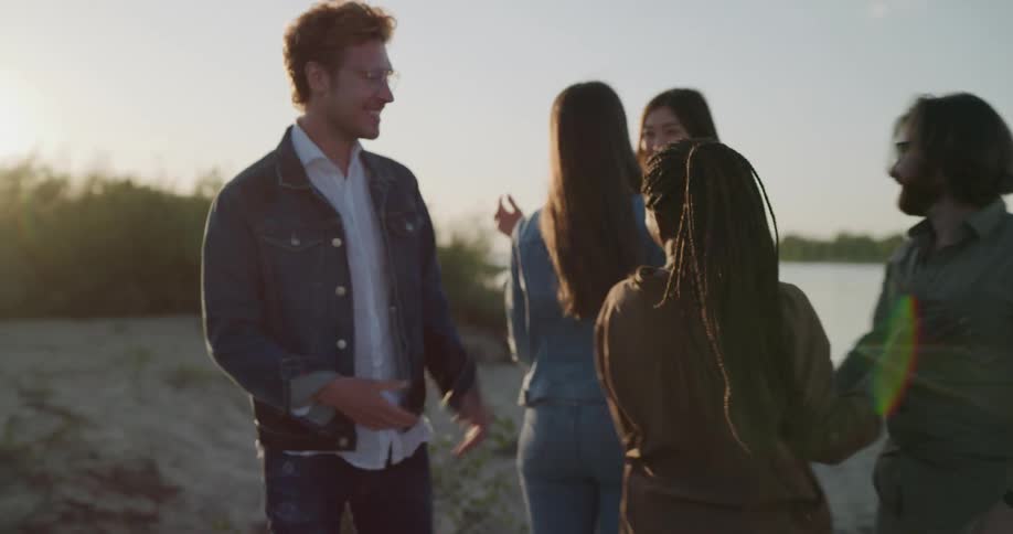 A woman walks with two men down a beach and they meet up with two other women and they all hug