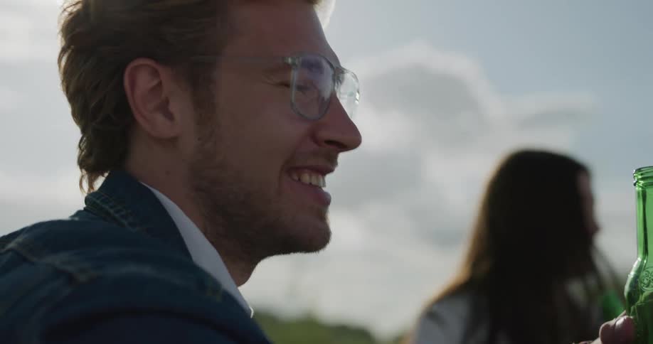 Man smiles and laughs while drinking beer with friends outside