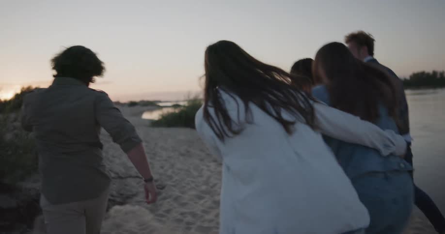 A group of friends are running on the beach at dusk
